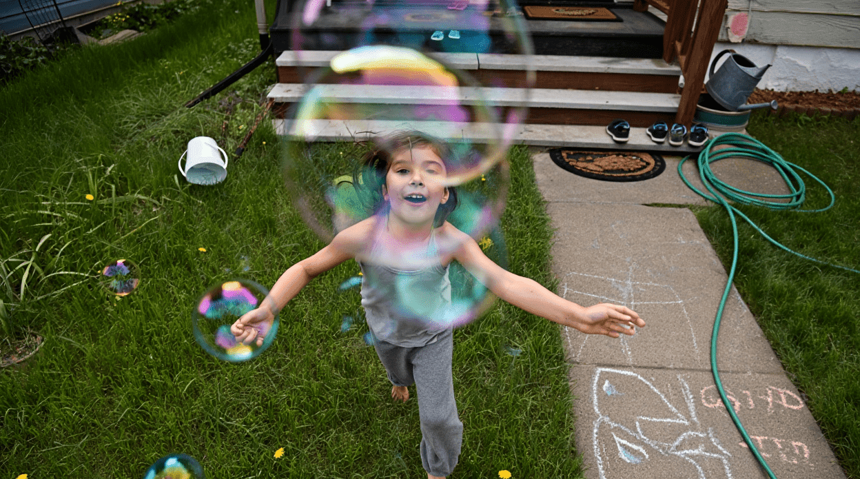 Child playing with bubbles in a grassy yard.